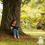Young person sitting under a large tree reading.